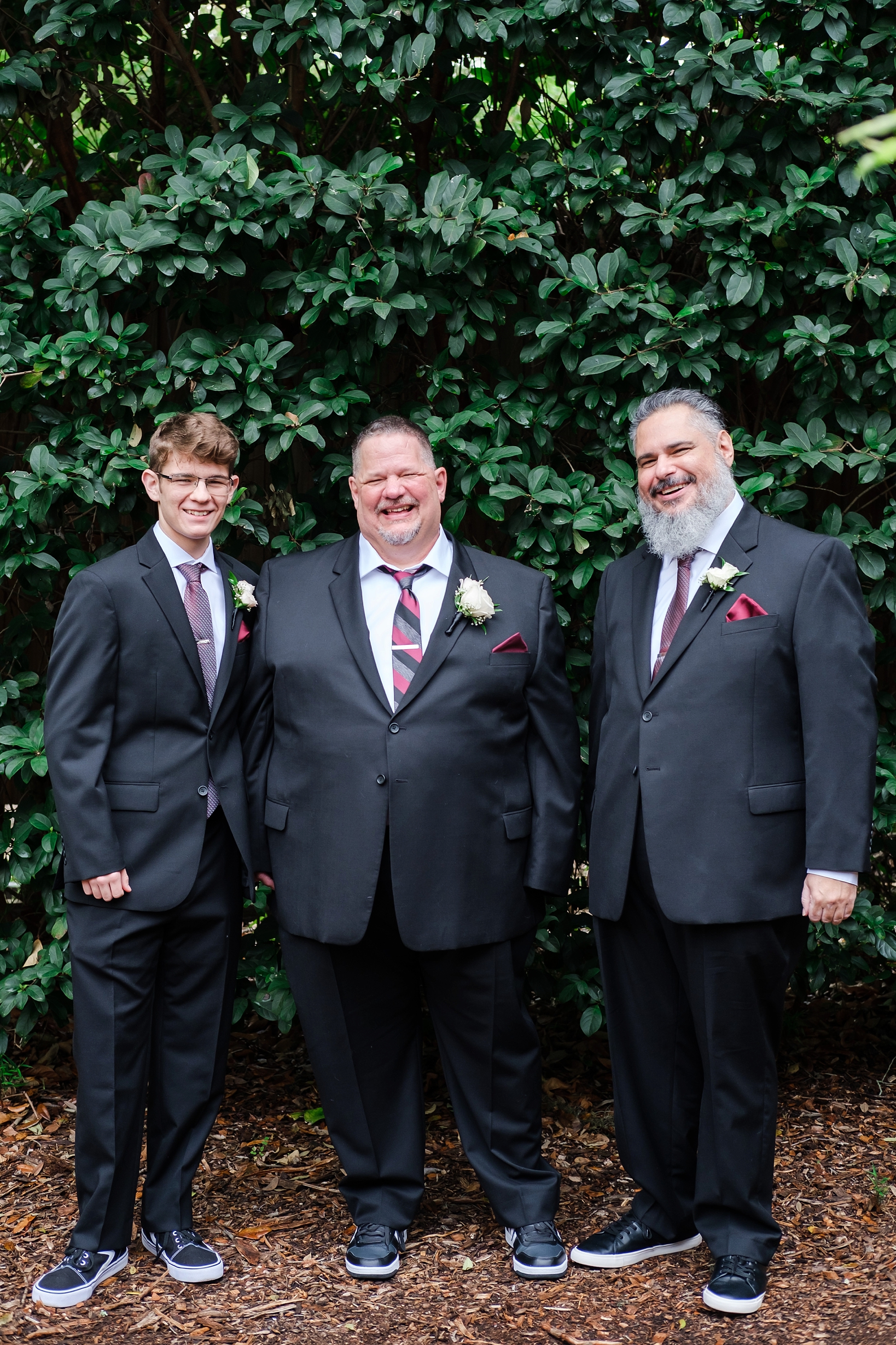 Groom and his Groomsmen in suits and sneakers pose for a formal portrait in front of large greenery