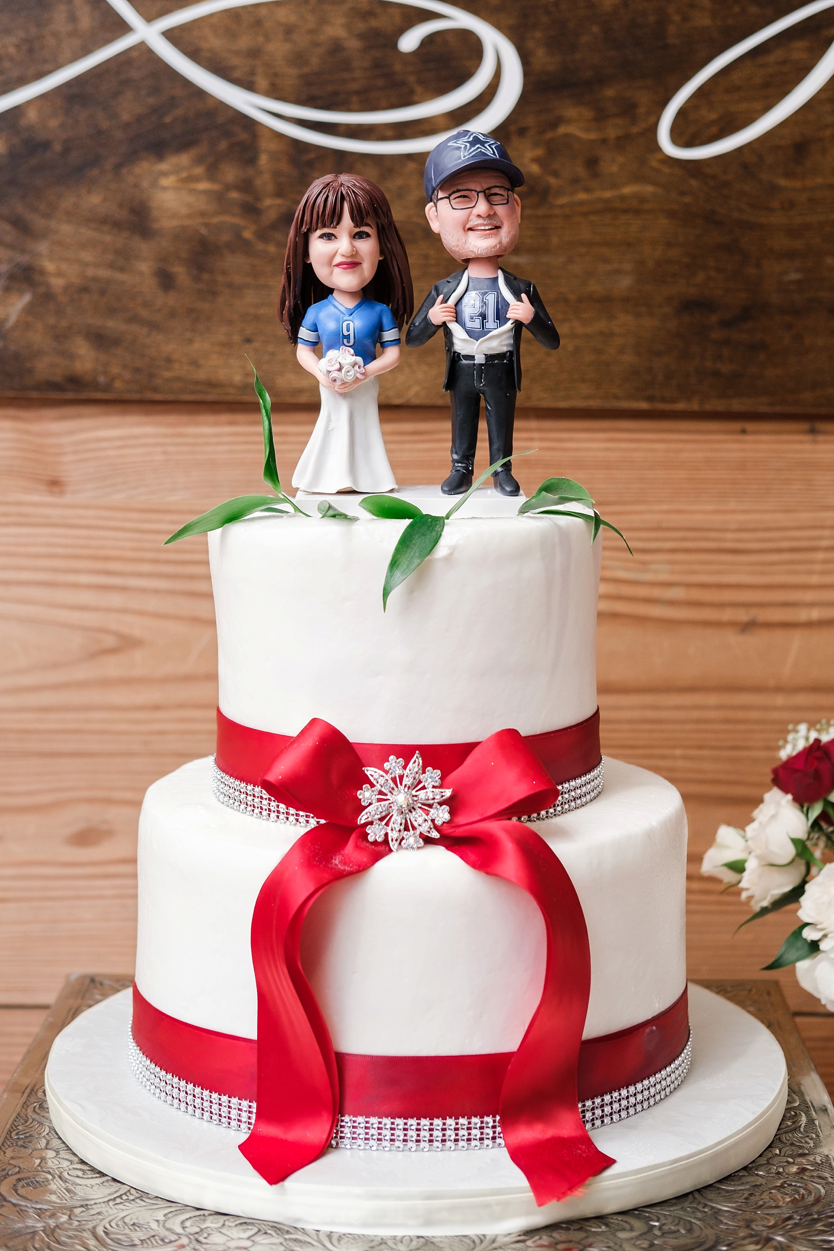 Custom made bobbleheads sit atop the wedding cake with bright red ribbon wrapping the base