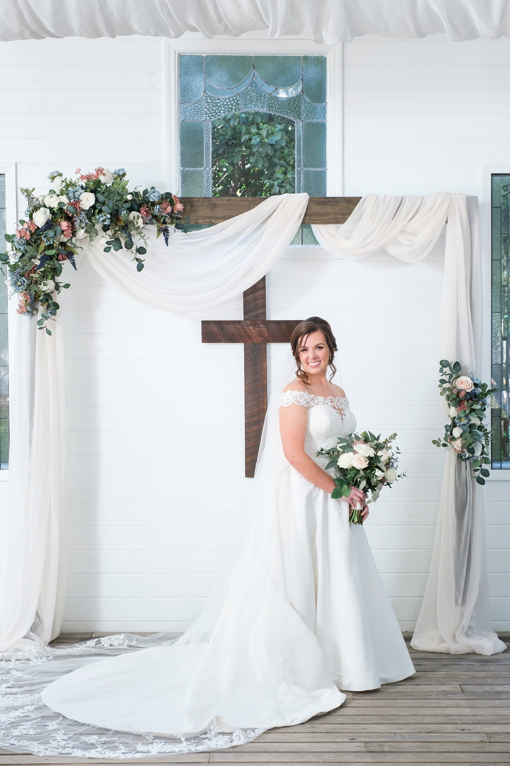 A portrait of the Bride standing up at the altar holding her floral bouquet