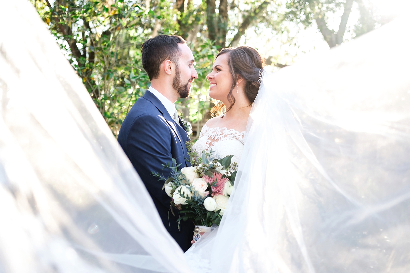 Bride and Groom smile at each other as the bridal veil blows in the wind