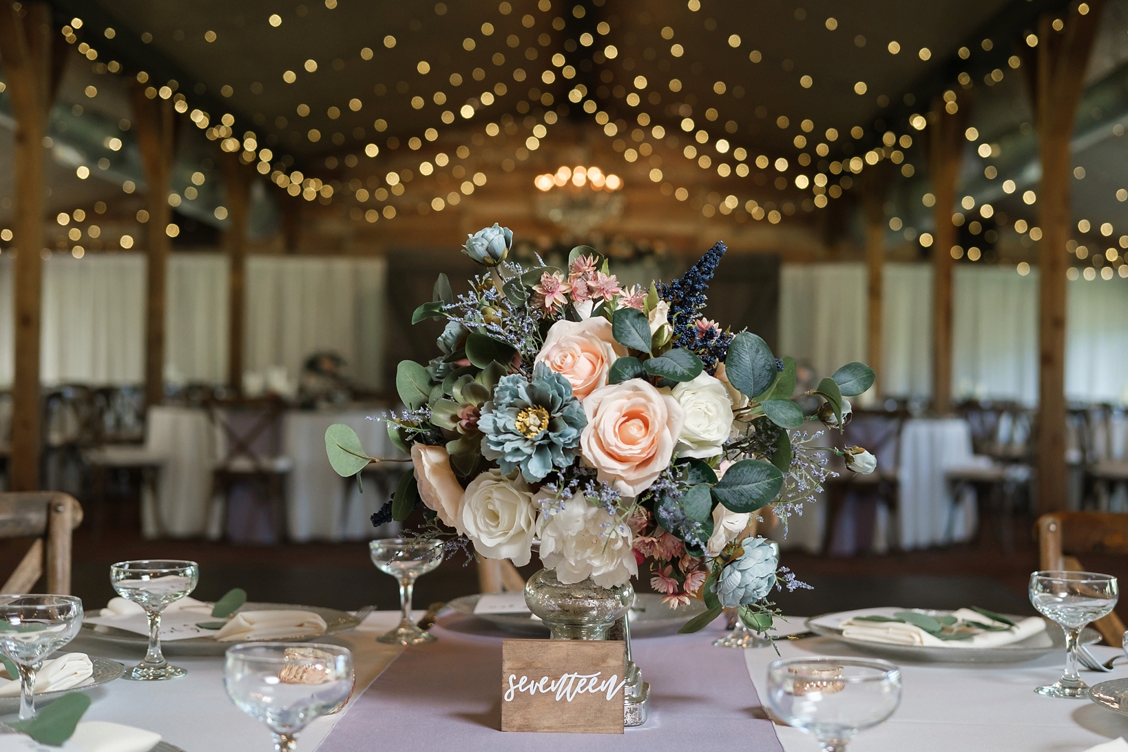A large floral arrangement and table number under the string lights of the wedding reception