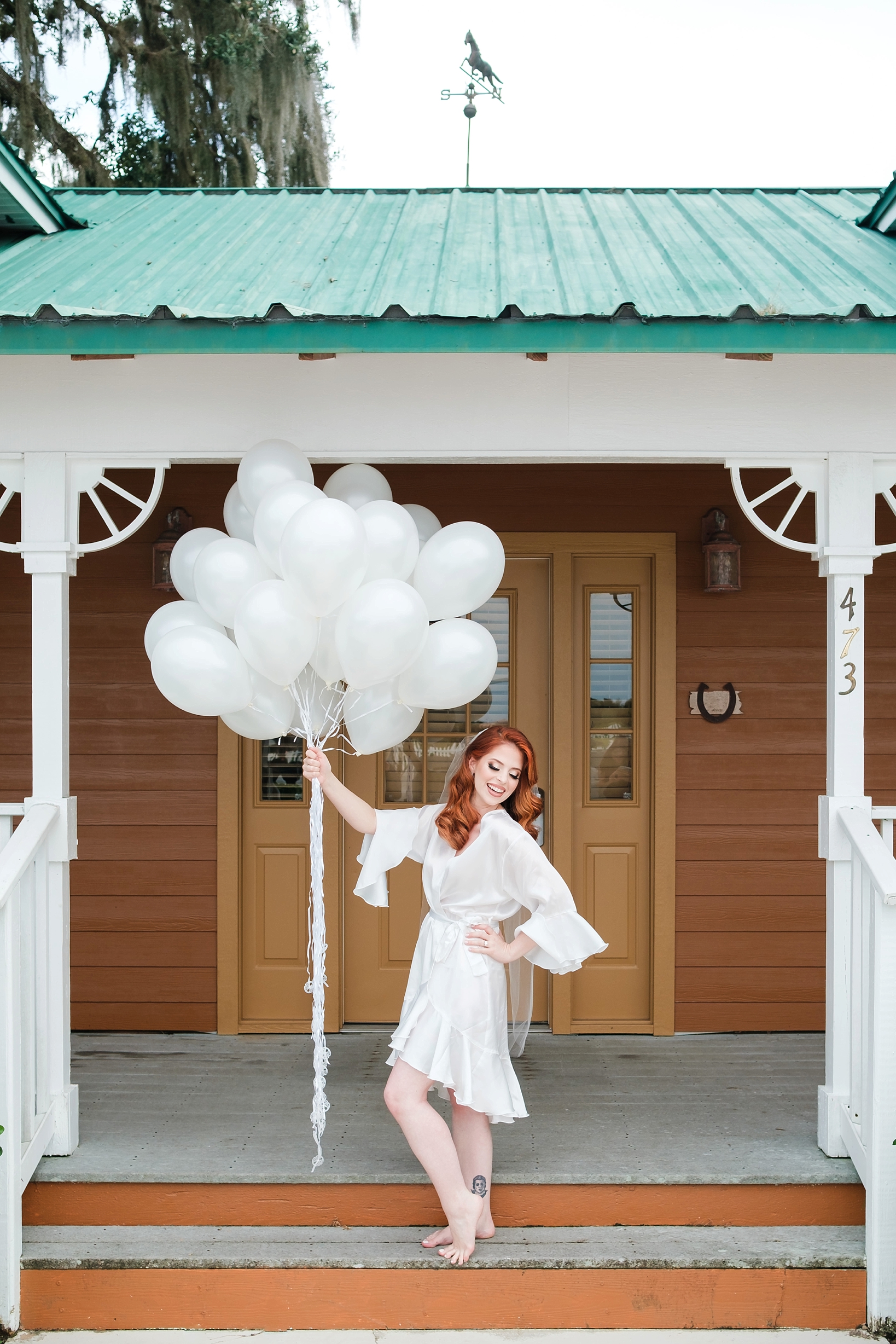 Bride holding a large bunch of white balloons outside of her suite before her Florida wedding