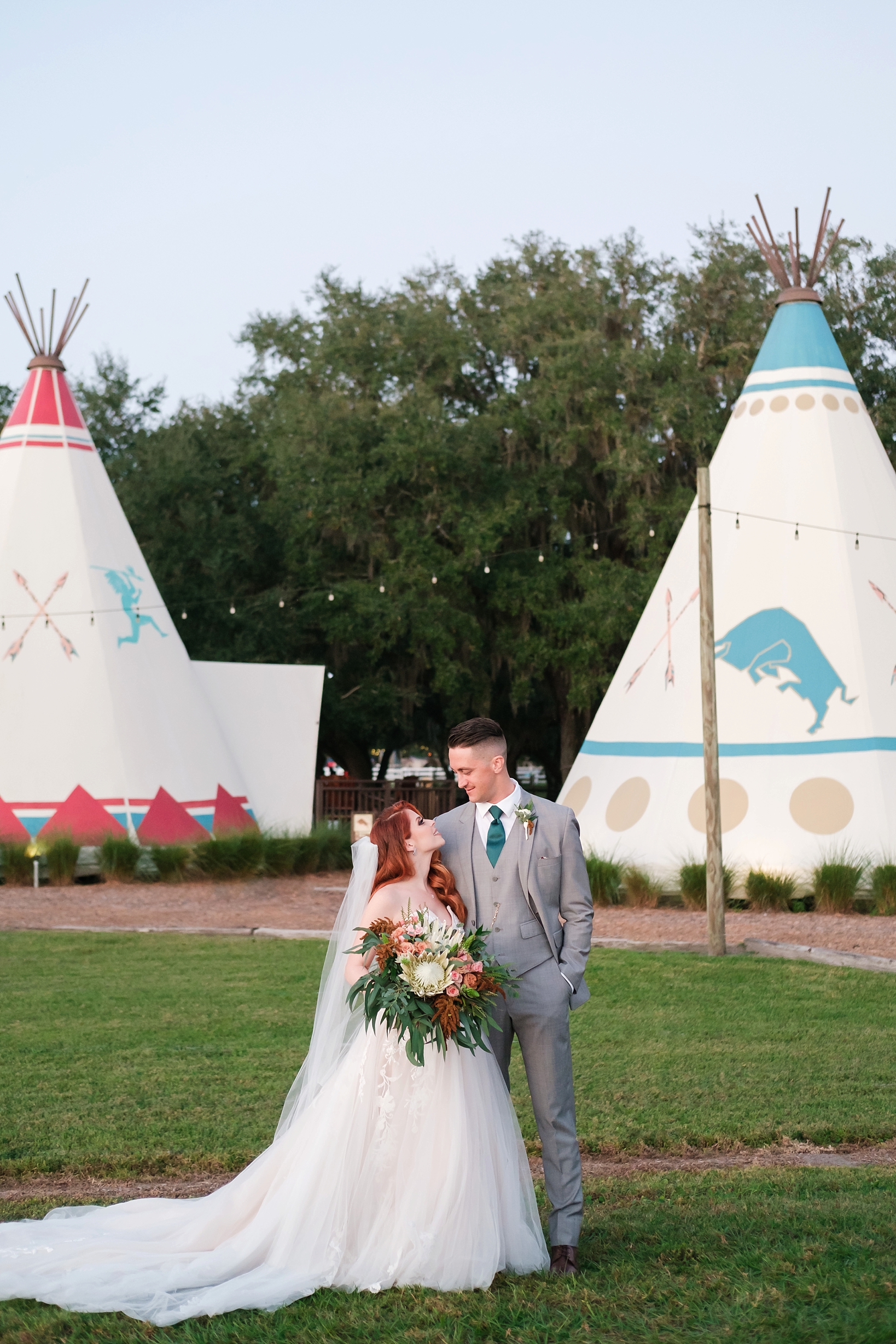 Bride and Groom pose in front of some stylised teepee's located at the Westgate River Ranch
