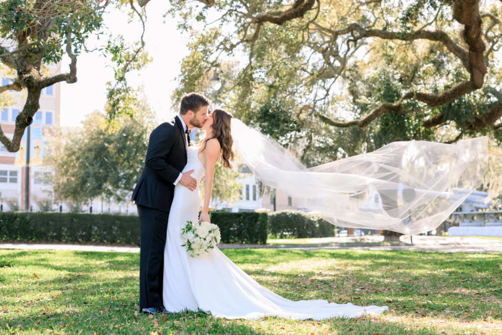 Bride and Groom kiss as the long veil blows in the wind captured by Sarah & Ben Photography