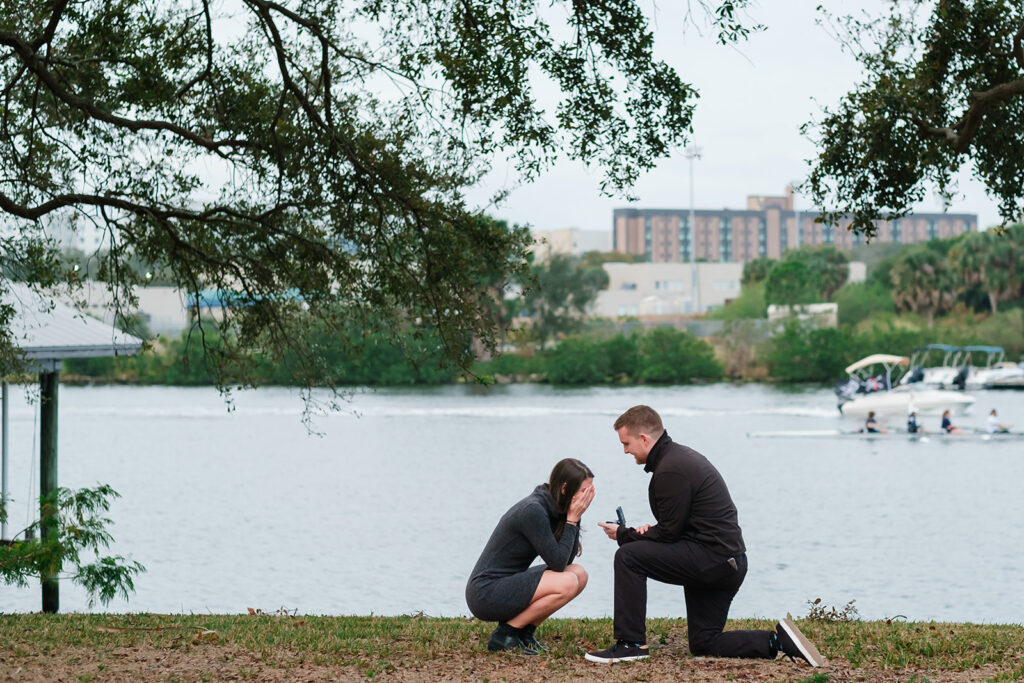 A man proposes down on one knee to his now fiancee on the bank of the Hillsborough River