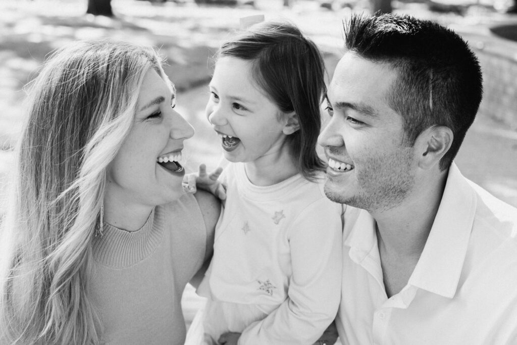 Black and White image of a Mom, Dad and Daughter laughing together