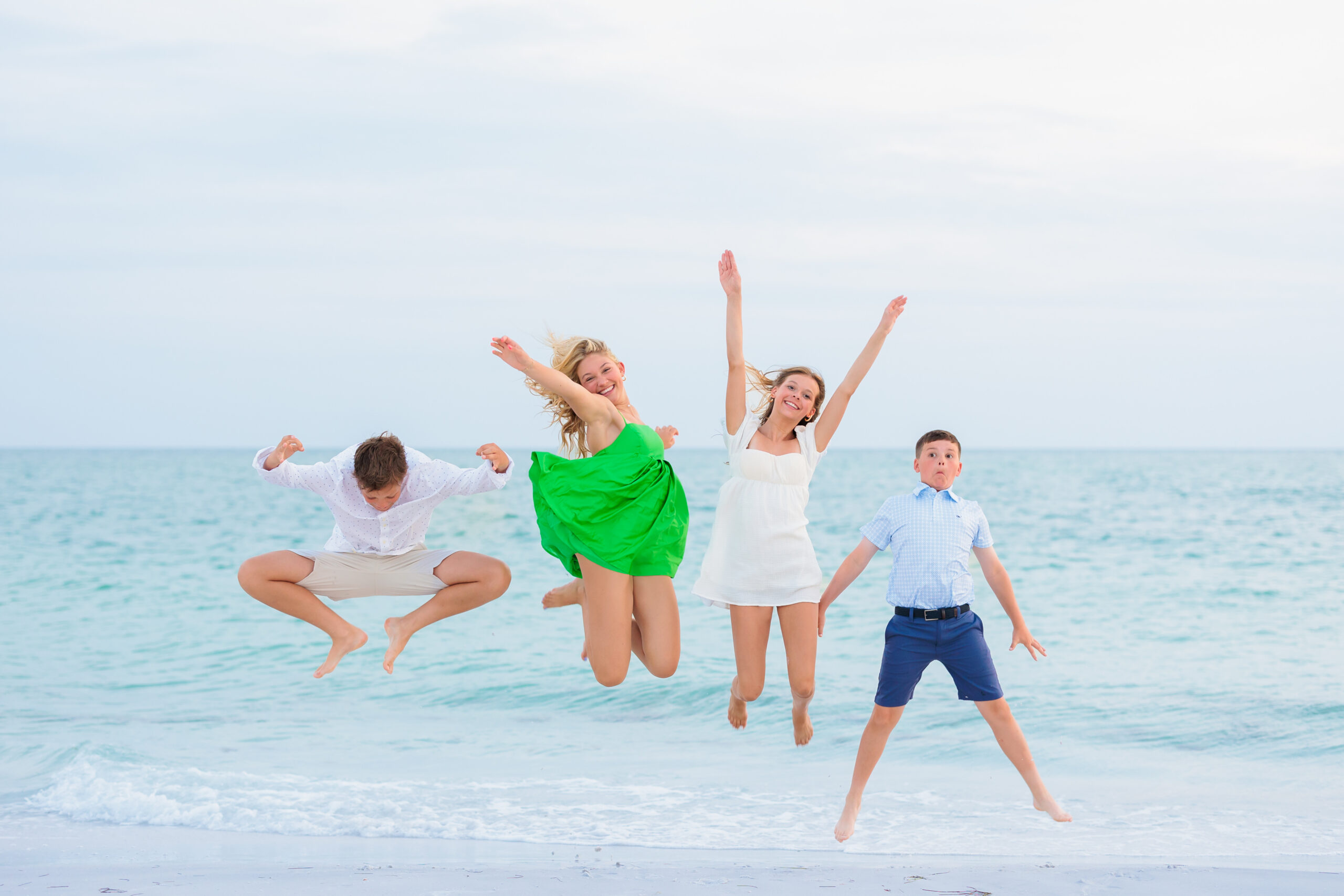 Four kids all strike a different pose as they jump in the air during their family beach photo session