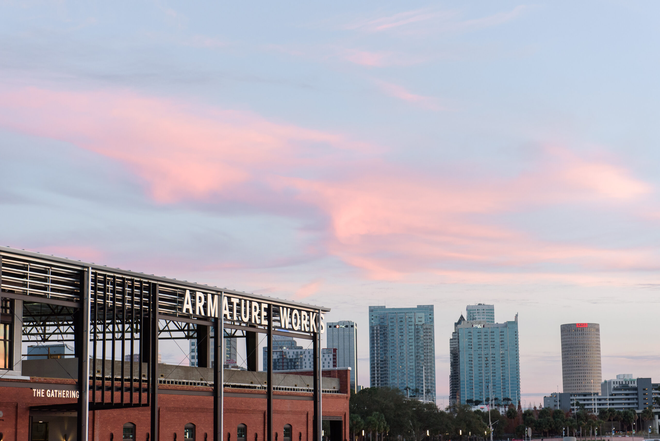 A picture of the Tampa skyline during sunset with the Armature Works building in the foreground.