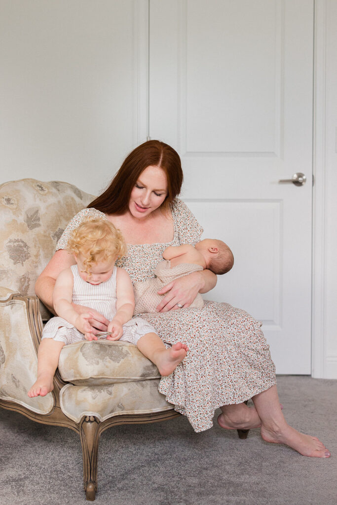 Mom sits with her newborn baby and toddler on a chair at home in Tampa Florida during a newborn session